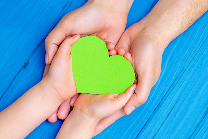 Aikuinen pitelee lapsen käsiä, lapsen käsissä on vihreä sydän.